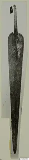 Long corroded metal blade with a tapering tang, photographed upright on a mounted card