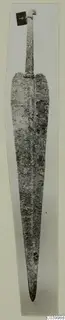 Corroded metal blade of a weapon from Lapithos Tomb 323 D, photographed upright on a pale background