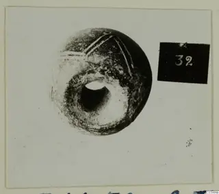 Round dark bead-like object with a large central hole and incised lines, from Lapithos Tomb 311 A
