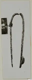 Corroded metal U-shaped implement with pointed ends, photographed on a pale card, from Lapithos Tomb 311A