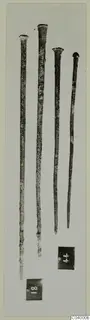 Four long slender bronze rods with flattened heads, photographed on a pale card with two number labels
