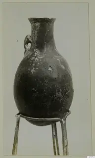 Red Polished III jug from Lapithos, standing on a three-legged wire stand against a plain background