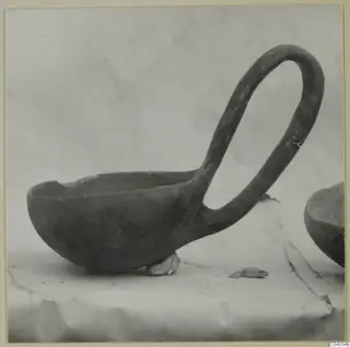 Red Polished III bowl with a tall loop handle, photographed in side view on a draped cloth.