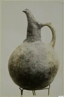 Round-bodied jug with a tall trefoil-type neck and one loop handle, standing on a wire stand.