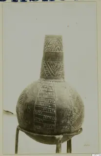 Pottery Red Polished II jug with incised geometric bands, shown on a three-legged metal stand