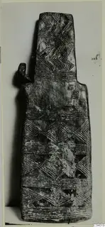 Flat idol-like object with incised chevron and band patterns, shown upright against a plain background