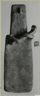 Terracotta idol, tall and flat, with incised bands and a small limbed figure clinging to its upper body