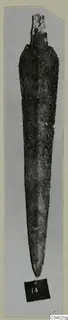 Long tapering bronze blade with a short squared end, photographed upright on a grey card mount