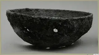 Rough-surfaced bowl with a thick rim and small openings in its side, photographed from the side
