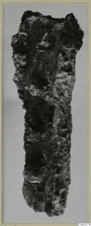Corroded iron tool, long and narrow, shown upright against a pale grey background
