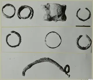 Corroded metal rings, a bent pin with a loop and an encrusted lump, laid out on a pale grey ground with a scale bar