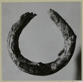 Corroded open metal ring from the Kastros tombs at Lapithos, photographed on a grey background.