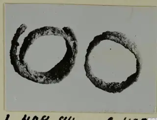 Two rings of metal, one open with overlapping ends, on a grey card mount
