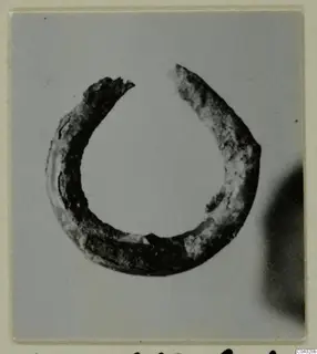 Single open ring of dark, corroded metal photographed against a grey background