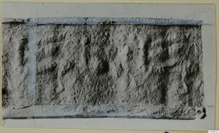 Rectangular grey stone object with incised marks or signs, edges taped in blue