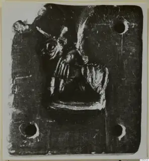 Square dark stone plaque with a raised figure in relief at its centre and holes near the corners