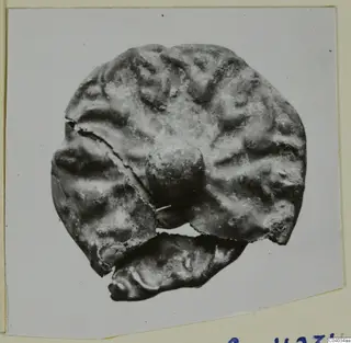 Corroded silver object, round and lumpy with a central knob and broken edges, shown on a photo card