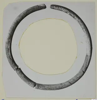 Open ring of silver with a round section, photographed on a grey card with a circular cut-out.