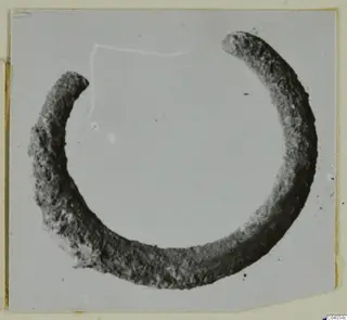 Corroded silver ring with a gap between its two ends, photographed on a grey card