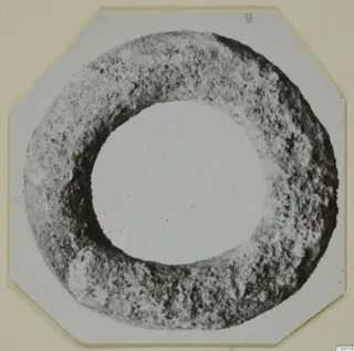 Lead ring-shaped object with a rough, pitted surface, seen face-on against a white card.