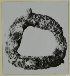 Corroded metal ring with a small knob on its upper edge, shown face on against a plain pale background.