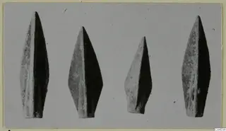 Four leaf-shaped metal weapon points standing in a row, tips upward, against a plain grey background.