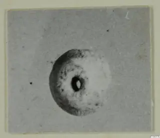 Small ring-shaped object with a central hole, shown in a photograph mounted on a cream card border