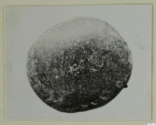 Round small find from Idalion, dark and mottled, photographed against a pale background.