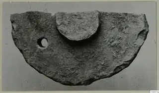 Half-disc shaped stone object with a small hole near one edge and a raised semicircular block on top