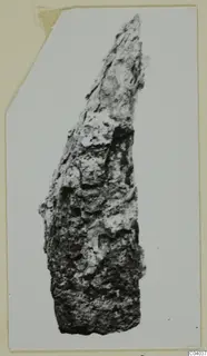 Corroded iron tool fragment, long and narrow, tapering to a point, shown on a photo mount