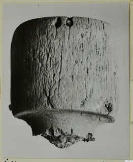 Cylindrical bone object with a wide flange near the base and a broken, crumbly lower end