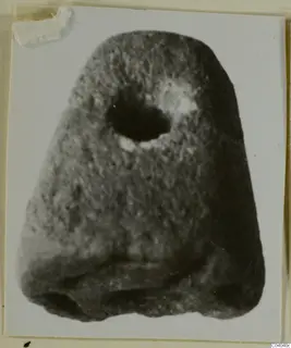 Stone object with a rounded top and a large hole near the upper part, photographed on a card mount
