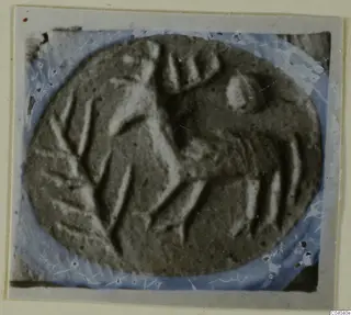 Oval engraved stone gem with carved lines, photographed on a light card mount with a blue-tinted border
