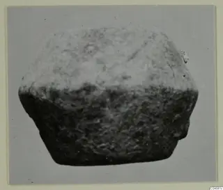 Small find: a squat, block-like object with a rough, granular surface, photographed against a grey background