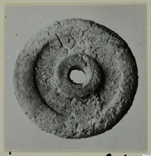 Flat disc-shaped bone object with a central hole, photographed from above against a grey backdrop