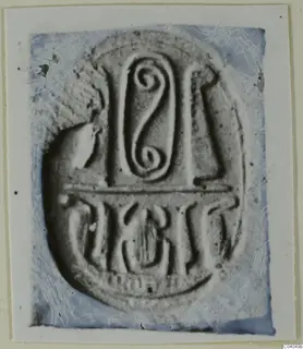 Oval seal or gem face with a spiral motif at the top, a horizontal bar and a row of incised signs below