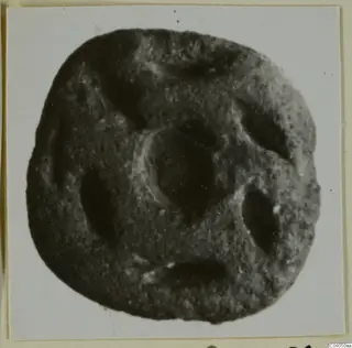 Glyptic object of stone with a rounded square outline, a central circular recess and four elongated hollows.