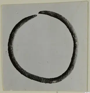 Open bronze ring or bracelet with a gap at the top, photographed on a grey card