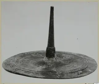 Bronze object: a flat circular disc with a tall tapering spike rising from its centre