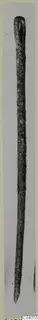 Long slender corroded metal object with a looped top and pointed tip, photographed upright, from Idalion.