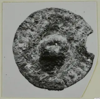 Round, corroded bronze mounting fragment with a raised central boss and a notch broken from its right edge.