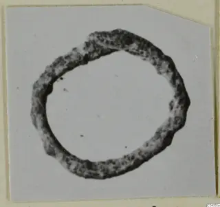 Bronze ring with a corroded, pitted surface, photographed flat on a pale card.
