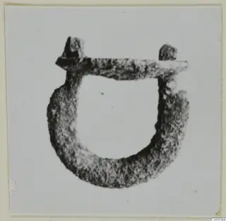 Corroded metal loop mounting with a bar across the top and a stub at each end, shown on a light card.