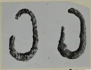 Two corroded curved bronze personal adornments, shown side by side.