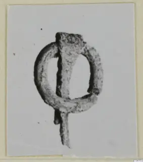 Small corroded bronze loop with a bar fixed across it, photographed on a pale card.