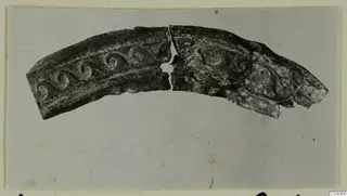 Curved metal fragment in two joined pieces, with raised spiral scroll decoration along its band, from Idalion