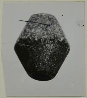 Faceted stone object with a hole in its base, photographed against a pale card background