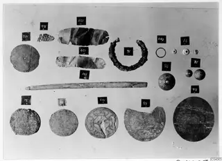Bronze Age small finds from Enkomi Tomb 6 laid out in rows, with discs, a ring, a rod, beads and number cards