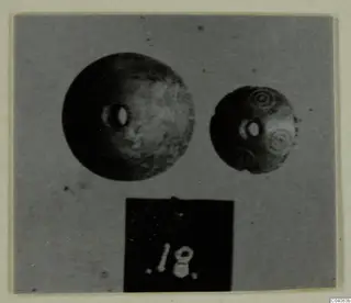 Two round jewellery objects with central holes, one plain and one with concentric circle decoration, shown with a number label