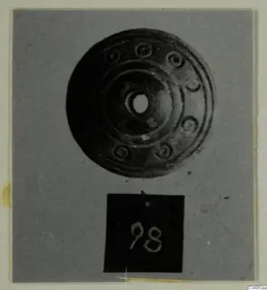 Disc-shaped object with a central hole and concentric rings, from Enkomi Tomb 6, shown with a number label.
